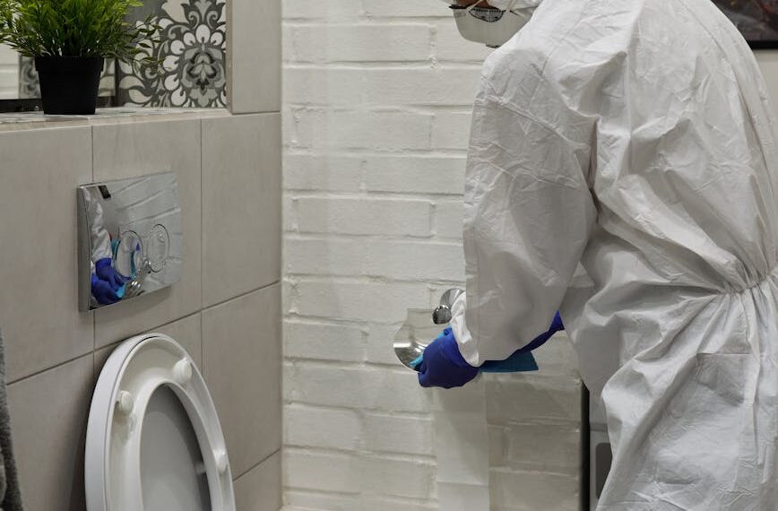 a person in white coverall sanitizing the toilet bowl