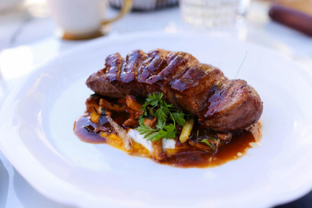 Deliciously roasted beef steak topped with herbs and sauce on a plate, perfect for gourmet dining.