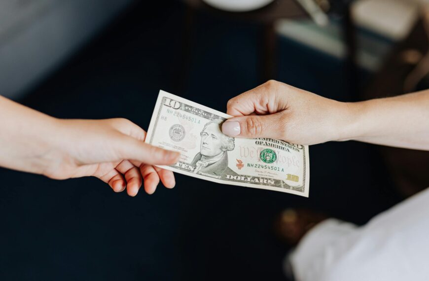 Two people exchanging a ten dollar bill in a close-up hand-to-hand transaction.