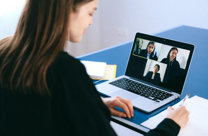 A woman engaging in a video conference using a laptop at home, taking notes.