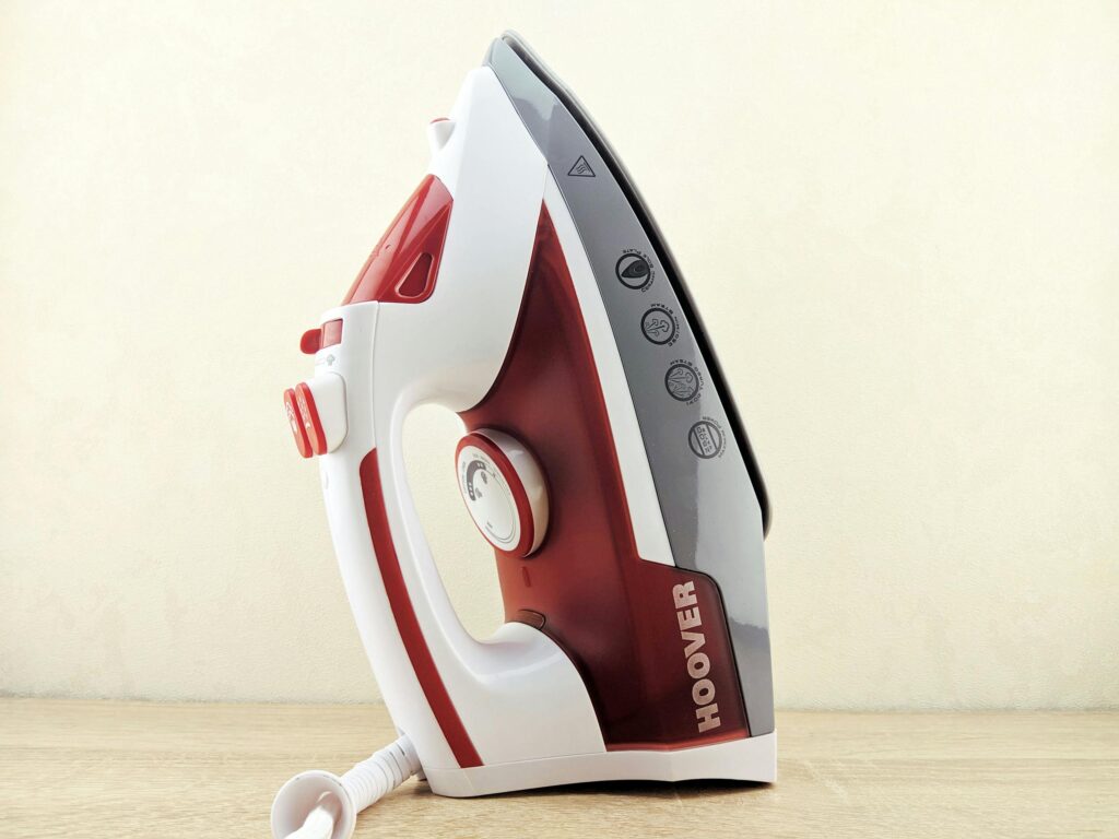 Contemporary multi functional wired iron of white and red colors placed on heel rest on white surface