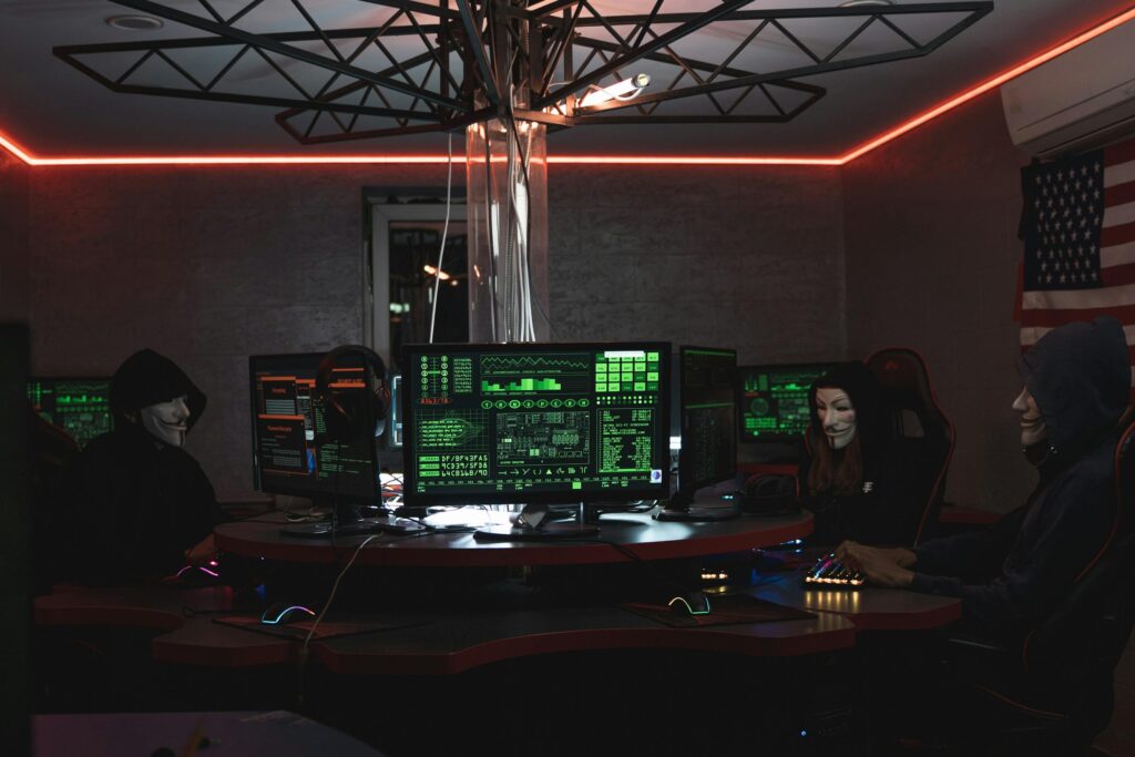 Team of hackers with Guy Fawkes masks coding in a dark room with computers.