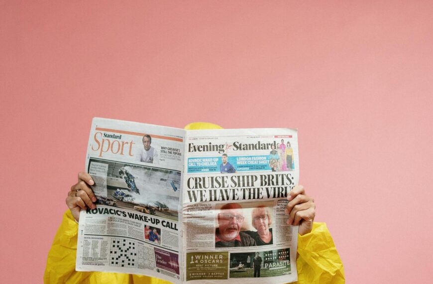 Individual in protective suit reads newspaper with pandemic headline against pink backdrop, symbolizing COVID-19 era.