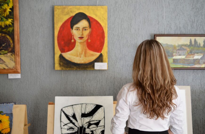 A woman views paintings in an art gallery, appreciating various art styles on display.