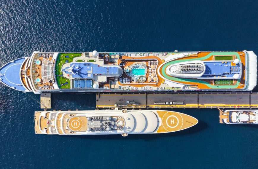 Top-down view of two luxurious cruise ships moored at a sunny port, showcasing pools and helipads.