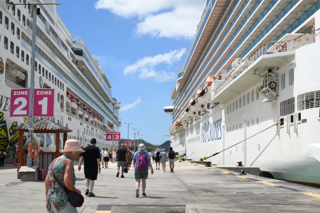 Bustling cruise port with tourists, featuring two large cruise ships under a bright blue sky.