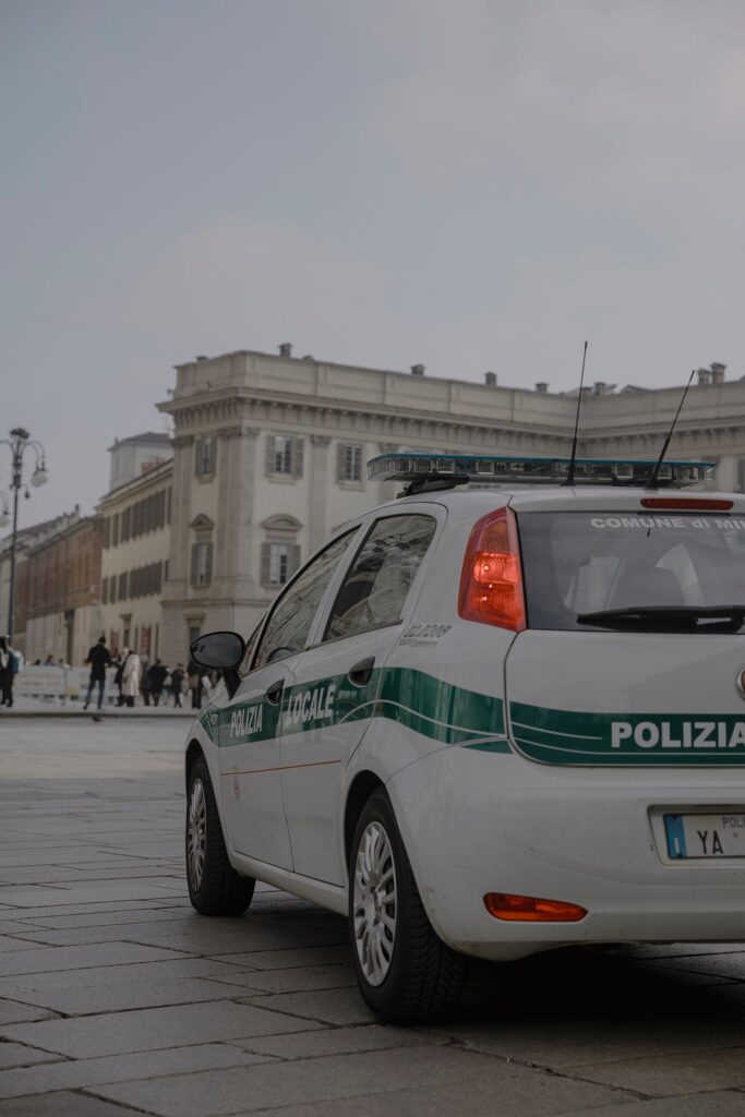 Italian police car parked in a busy Milan square with historical architecture.