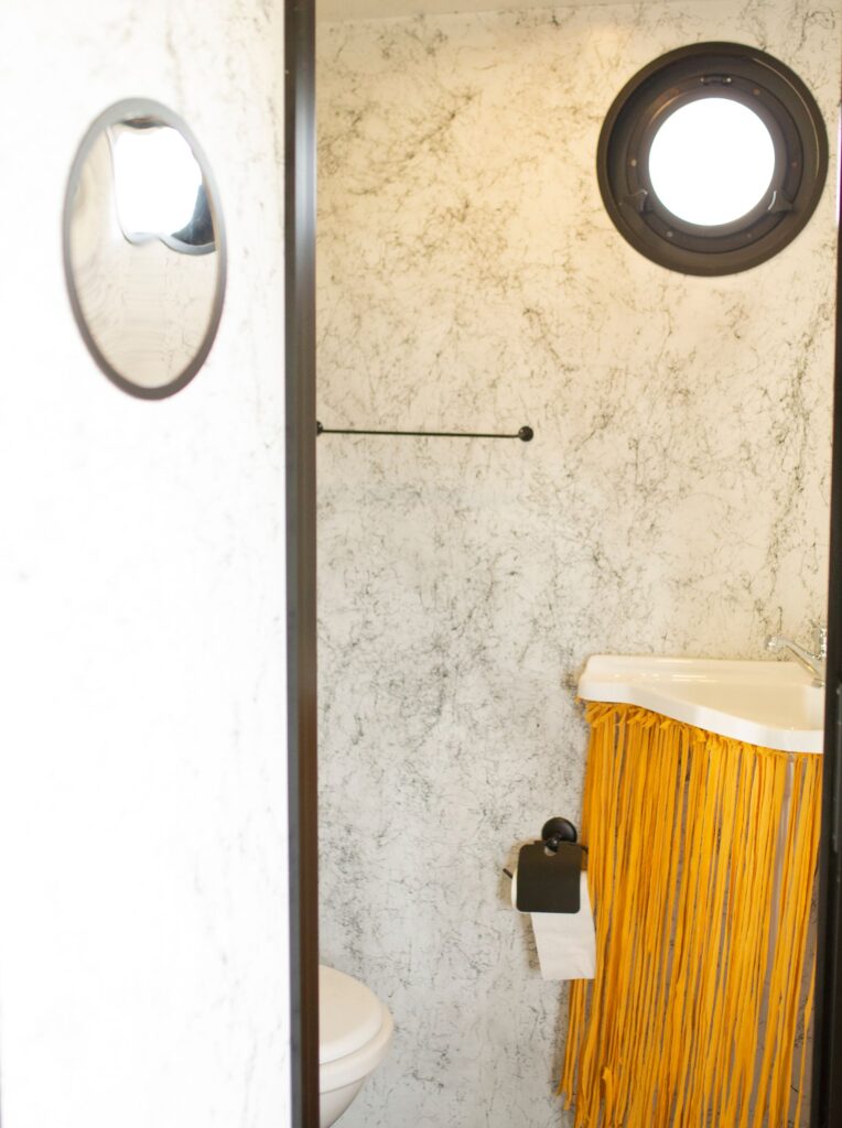 Stylish bathroom featuring a marble wall, round window, and unique fringe decor on the sink.