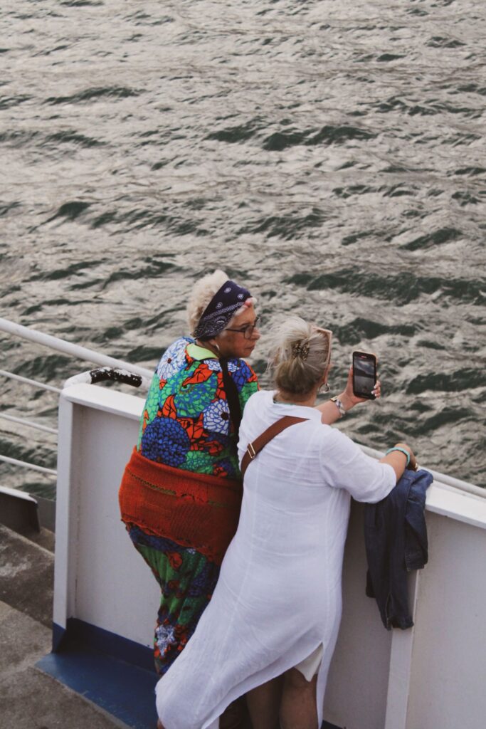 Two women taking photos on a ferry with a smartphone view of a river.