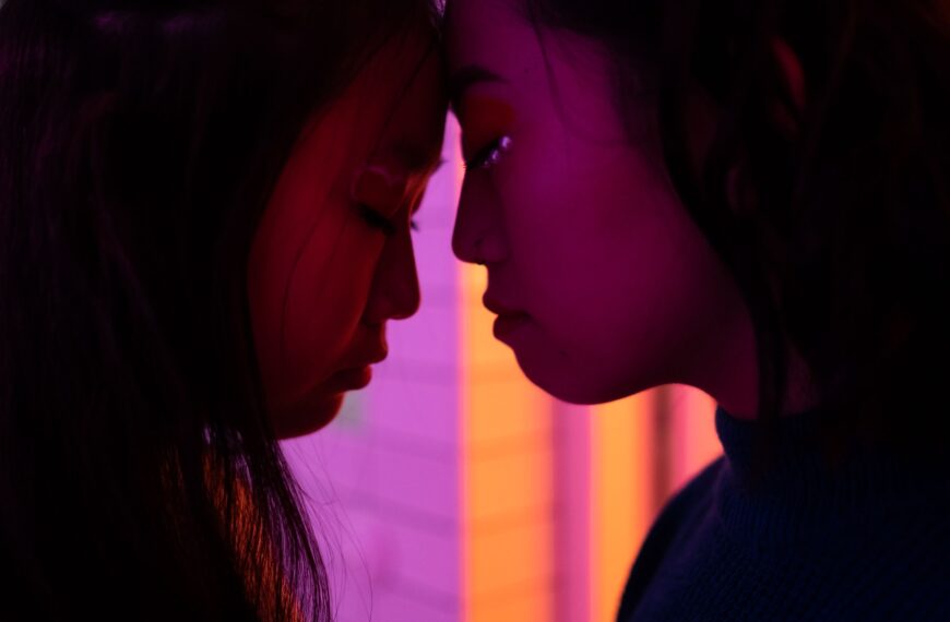 Intimate profile of two women touching foreheads bathed in vibrant neon light.